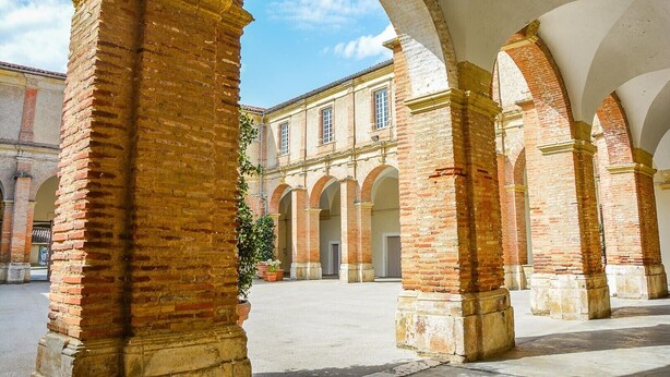 Une cour intérieure avec des arcades en briques et un bâtiment en arrière-plan.