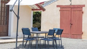 Une terrasse extérieure avec une table et des chaises, un parasol blanc et une porte rouge.