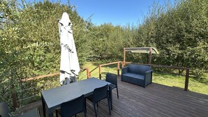 Een houten terras met een tafel en stoelen, een overdekte zithoek en een pergola.