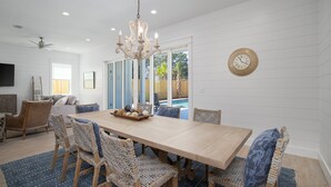 Uma sala de jantar ampla com mesa de madeira, cadeiras de fibra e lustre.