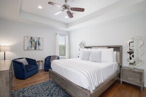 A bedroom with a large bed, a ceiling fan, a nightstand, a dresser, and a blue armchair.