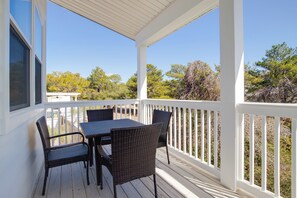 A covered outdoor area with a table and chairs, white railings, and a view of trees and sky.