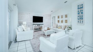 Una sala de estar moderna con muebles blancos, un televisor de pantalla plana y un ventanal grande.
