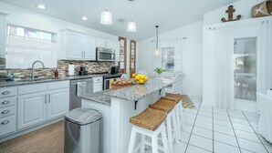 Una cocina moderna con armarios blancos, encimera de granito y una isla central con taburetes de bar.