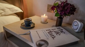 A bedside table with a book titled 'The Life Plan,' a cup of coffee, a candle, and a clock. - Host Stay Tin Bath (Langport)