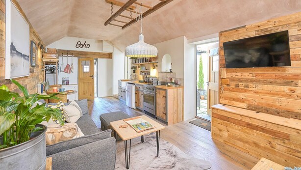 A spacious living area with a sofa, a dining table, a kitchen with wooden cabinets, and a large TV mounted on the wall.