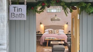 A bedroom with a bed, bedside tables, a hanging light fixture, a bench, and a sign reading 'Tin Bath'.