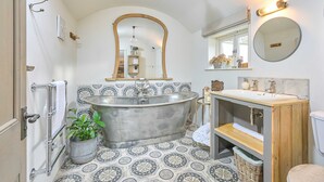 A bathroom with a freestanding bathtub, a wooden vanity, a round mirror, and patterned floor tiles.