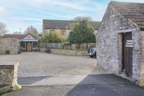A gravel courtyard with stone buildings, a wooden fence, and a parked car. - Host Stay Tin Bath (Langport)