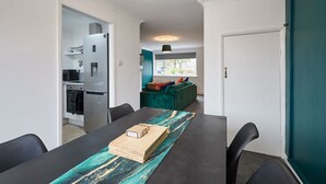 Une cuisine moderne dotée d’un réfrigérateur et d’un four encastrés, un coin repas avec une table et des chaises, et un canapé de couleur turquoise en arrière-plan.