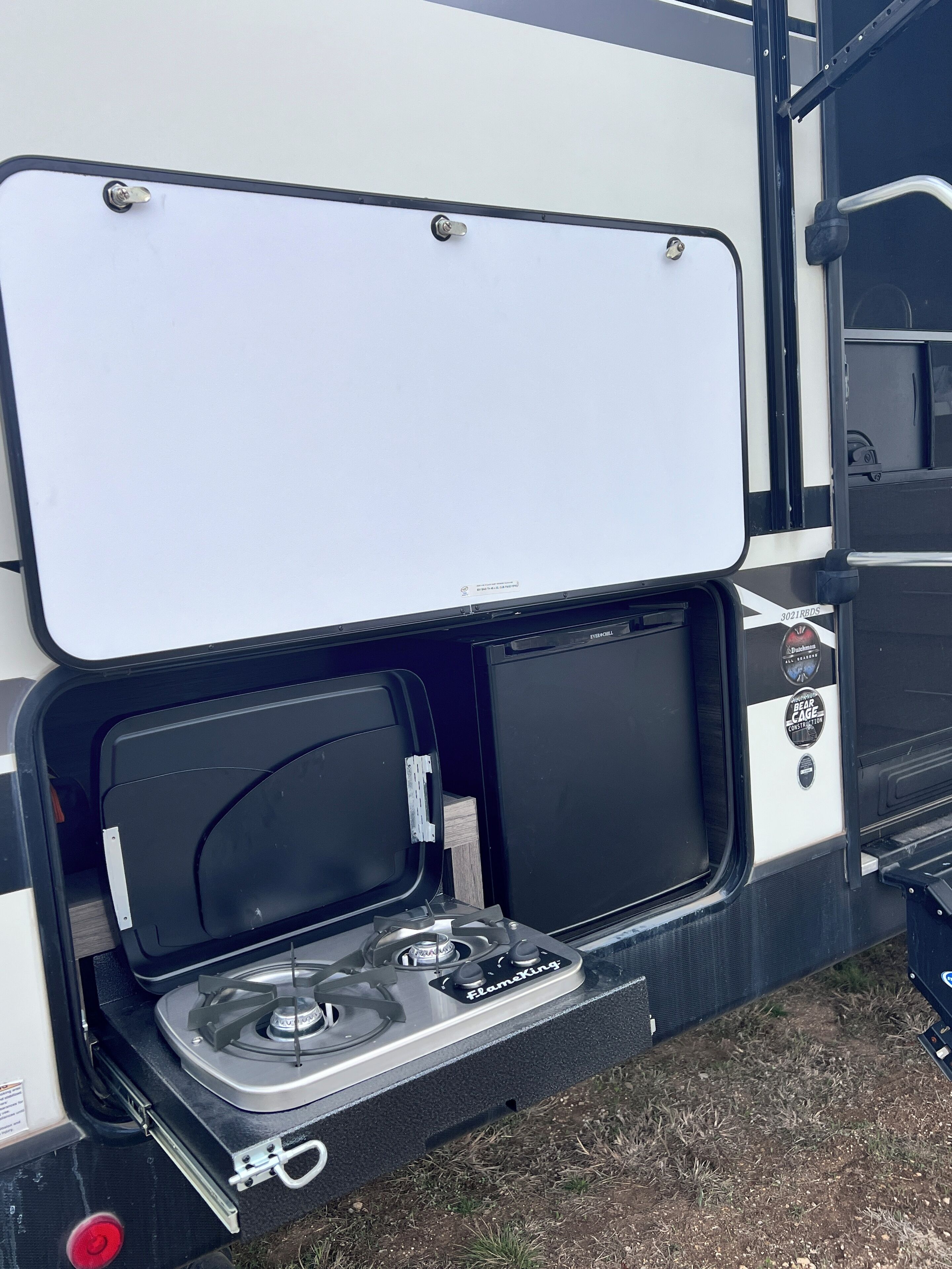 A travel trailer with an open kitchen area featuring a portable gas stove and a storage compartment.