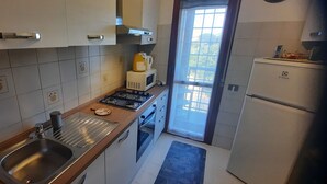 Una cocina compacta con muebles blancos, un lavaplatos de acero inoxidable, un microondas, una estufa y un refrigerador.