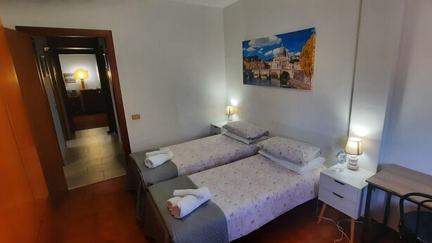 Habitación de hotel con dos camas, un escritorio, una silla, una lámpara y un cuadro en la pared.