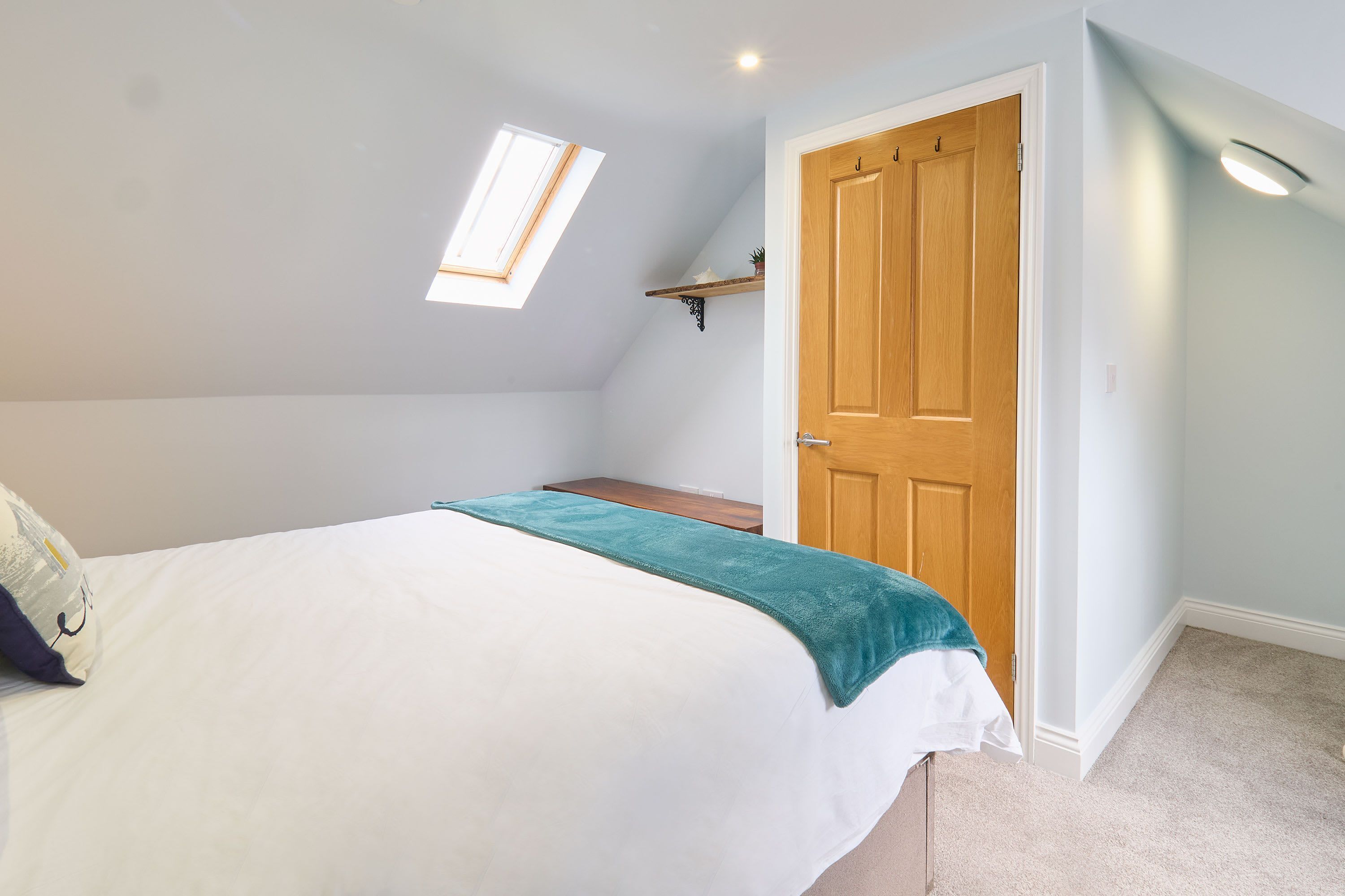 A bedroom with a bed, a skylight, a wooden door, and a shelf.