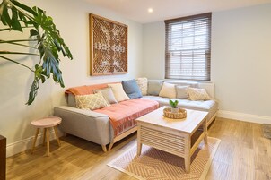 Una sala acogedora con un sofá gris, una mesita de noche rosa y una mesa de centro de madera.