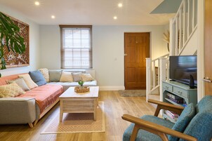 Una sala de estar con un sofá, una mesa de centro, un mueble para la televisión y una estantería.