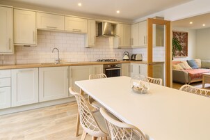 Una cocina moderna con armarios blancos, encimera de madera y comedor con mesa blanca y sillas de mimbre.