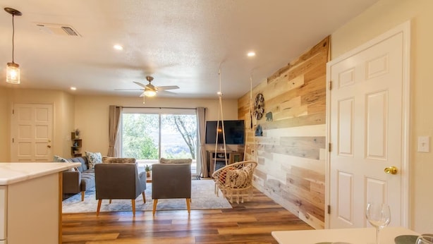 A spacious living area with a wooden floor, a sofa set, a dining table with a bowl and wine glass, and a TV mounted on the wall. - Peaceful Hillside Home with 3BD:2BTH & 30 Mins to Yosemite (Oakhurst)