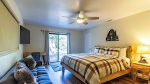 A bedroom with a bed, a desk, a chair, a ceiling fan, and a view through a glass door. - Peaceful Hillside Home with 3BD:2BTH & 30 Mins to Yosemite (Oakhurst)