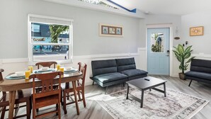 Ein modernes Wohnzimmer mit Essbereich, einer Couch, einem Couchtisch und Blick auf eine Autowaschanlage durch das Fenster.