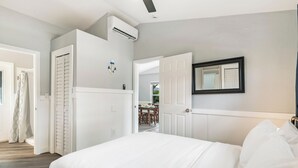 Ein Schlafzimmer mit einem großen Bett, weißen Wänden, einem Deckenventilator und einer Tür zu einem Essbereich.