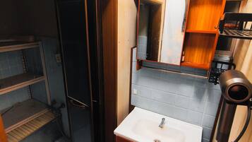 A compact bathroom with a wooden vanity, a sink, a mirror, and a hairdryer.