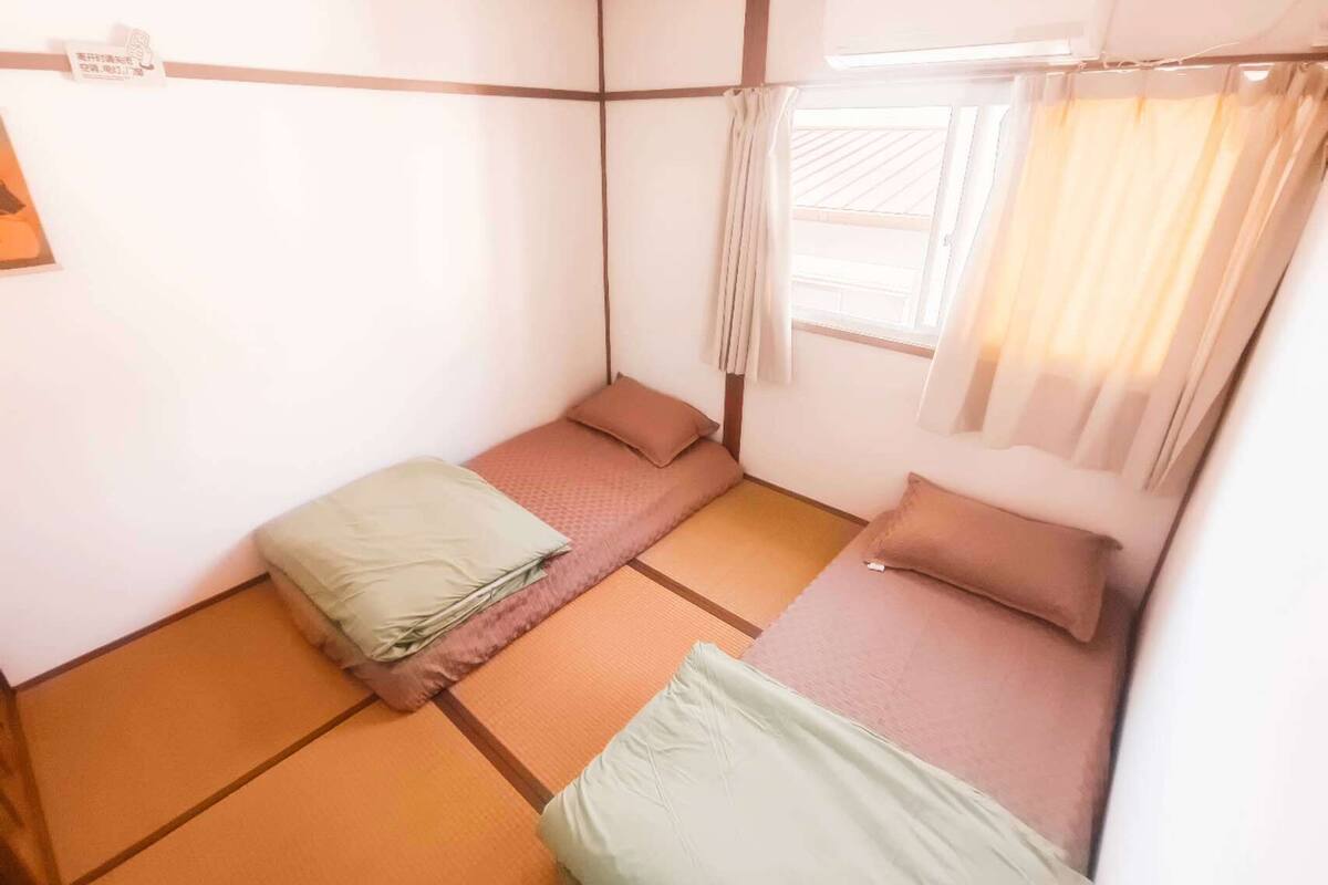 A small, traditional Japanese-style room with tatami flooring, a low bed with a pillow, and a window with curtains.