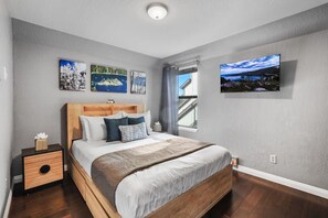 A bedroom with a bed, a nightstand, a window with a view, and wall art.