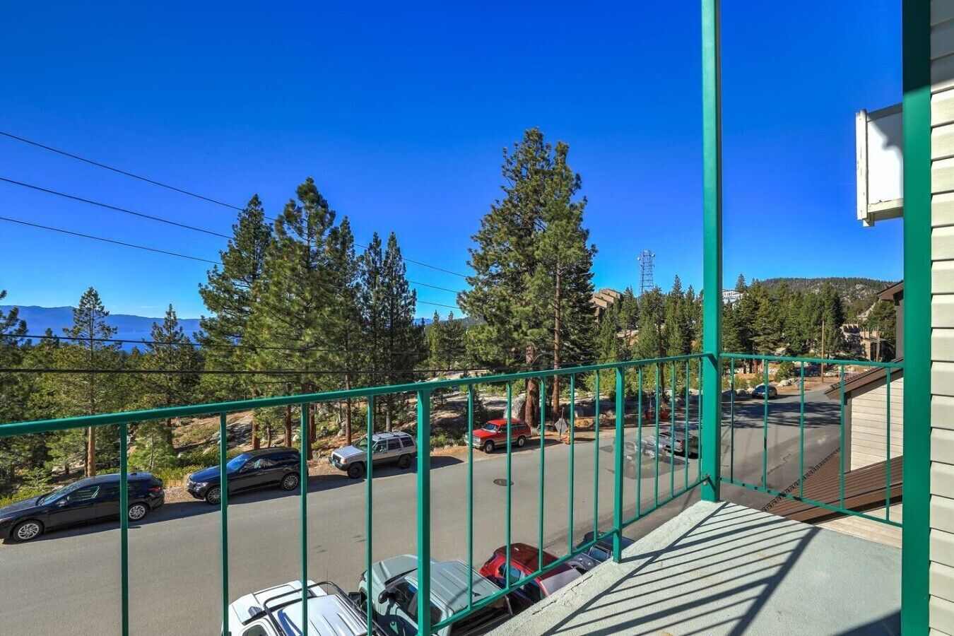 A balcony with a view of parked cars and trees, a clear sky, and a distant mountain range.