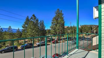 A balcony with a view of parked cars and trees, a clear sky, and a distant mountain range.