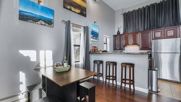A modern kitchen with a dining area, wooden bar stools, and a refrigerator.