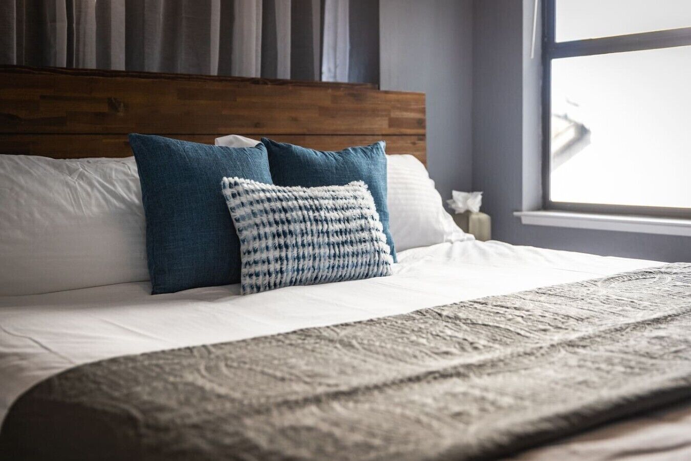 A neatly made bed with a wooden headboard, two pillows, and a textured blanket.
