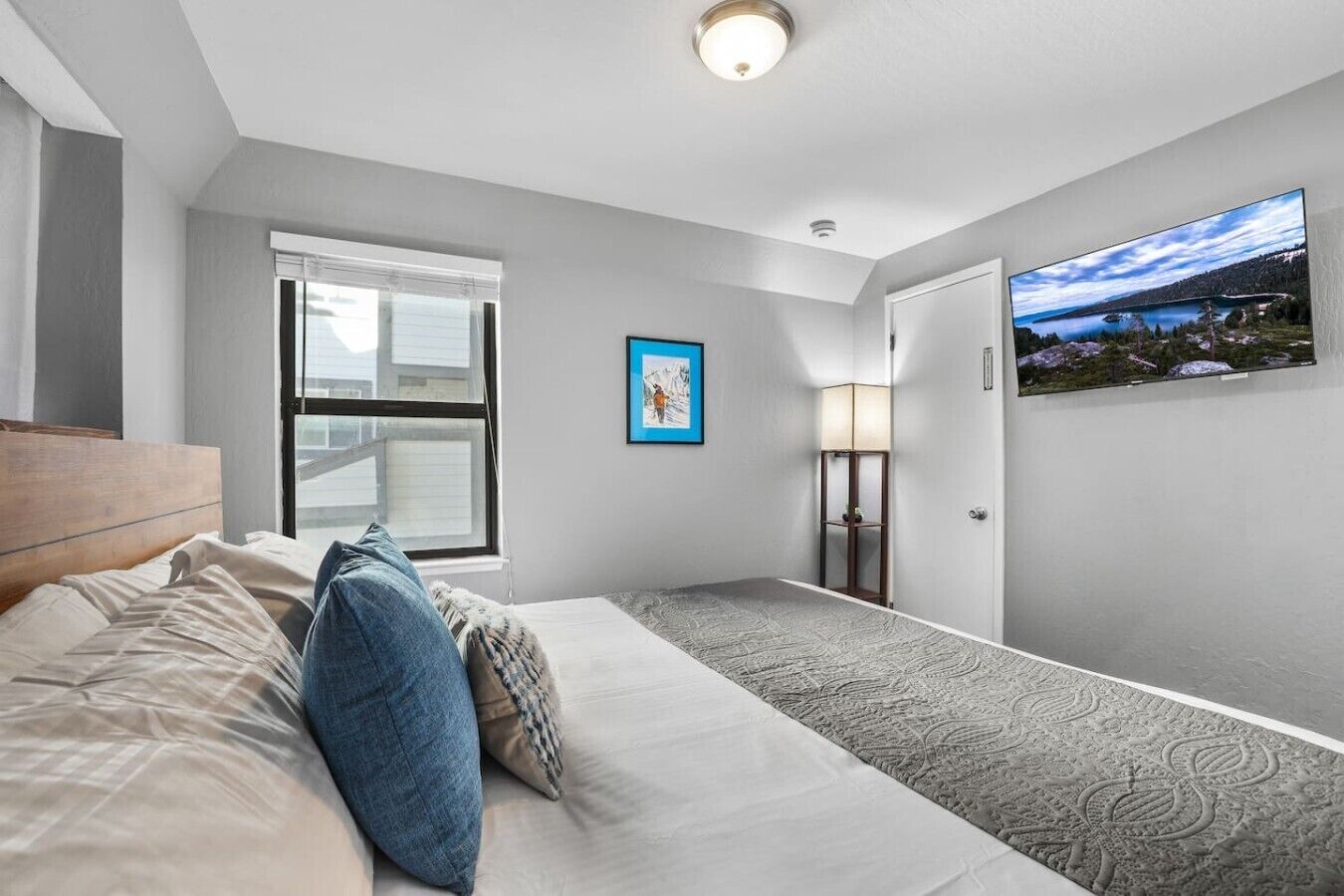 A hotel room with a bed, a window, a painting, a lamp, and a view of a landscape.