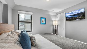 A hotel room with a bed, a window, a painting, a lamp, and a view of a landscape.