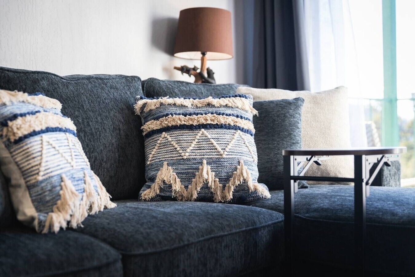 Un canapé bleu foncé agrémenté de trois coussins décoratifs, une petite table et une lampe, le tout dans une pièce offrant une vue agréable.