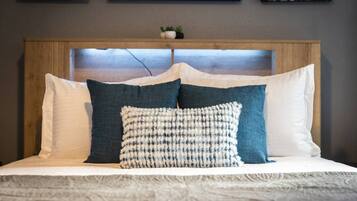 A bed with a wooden headboard, white and blue pillows, and a textured throw blanket.
