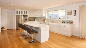 A modern kitchen with white cabinetry, a central island with bar stools, a large window, and a stainless steel refrigerator. - Bruny Horizon - Where the Country meets the Sea (North Bruny)