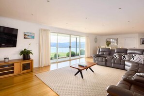 A spacious living room with a large window offering a scenic view, a leather sofa, a wooden coffee table, and a TV mounted on the wall. - Bruny Horizon - Where the Country meets the Sea (North Bruny)