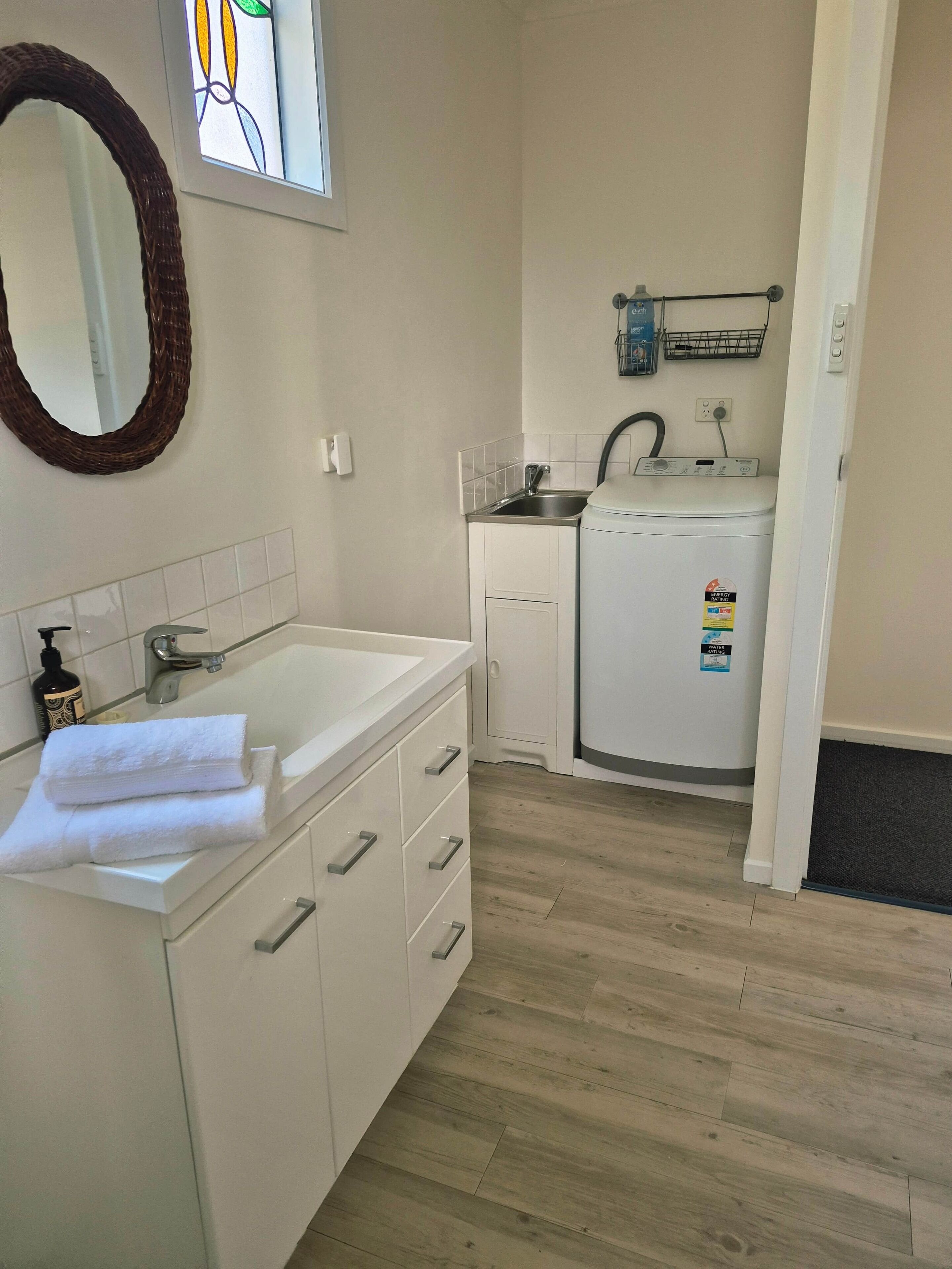 A modern bathroom with a white vanity, a mirror, a small sink, and a compact washing machine.
