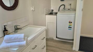 A modern bathroom with a white vanity, a mirror, a small sink, and a compact washing machine.