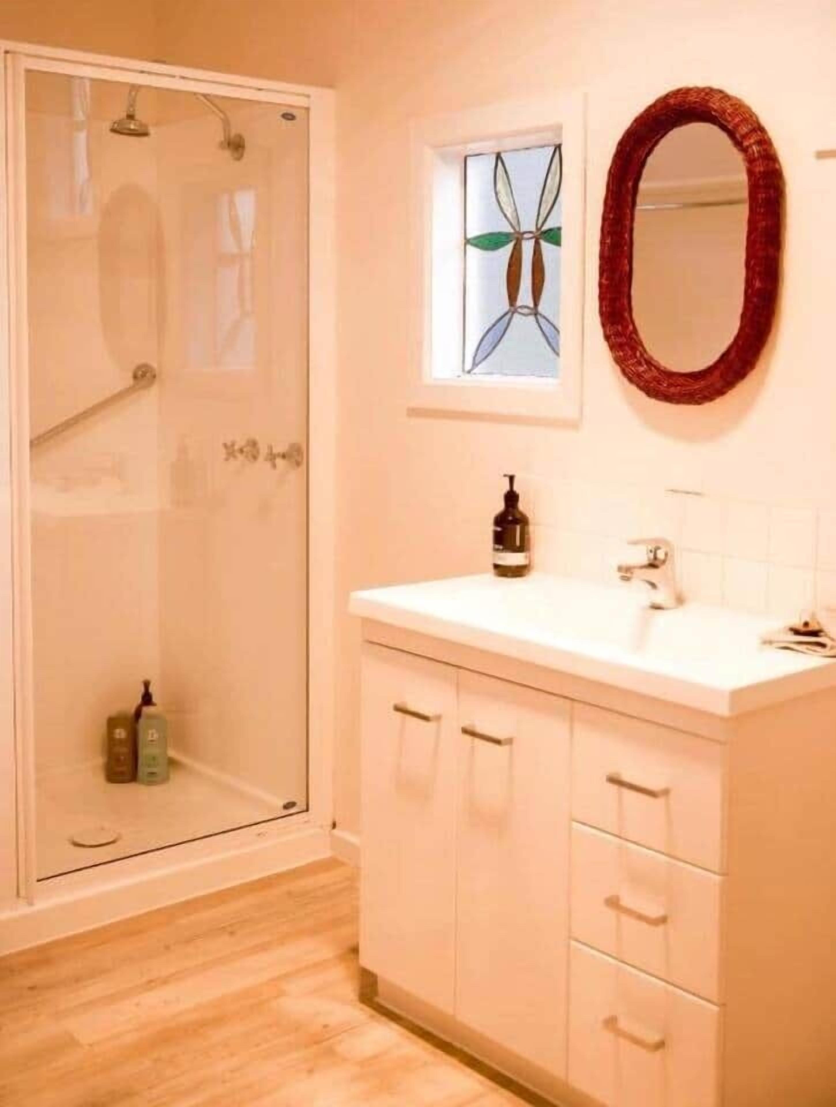 Een badkamer met een douchecabine van glas, een witte wastafel met spiegel en een klein raam met decoratief ontwerp.