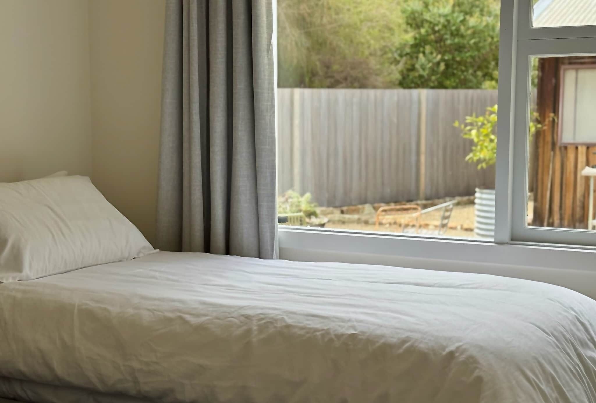A bedroom with a bed, a window, and a view of a backyard.