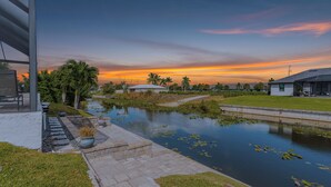 A serene riverside view with a modern house, a small bridge, and a grassy area.