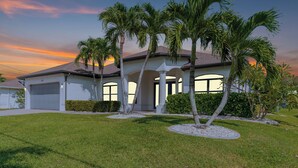 A two-story house with a garage, surrounded by a well-maintained lawn and palm trees.