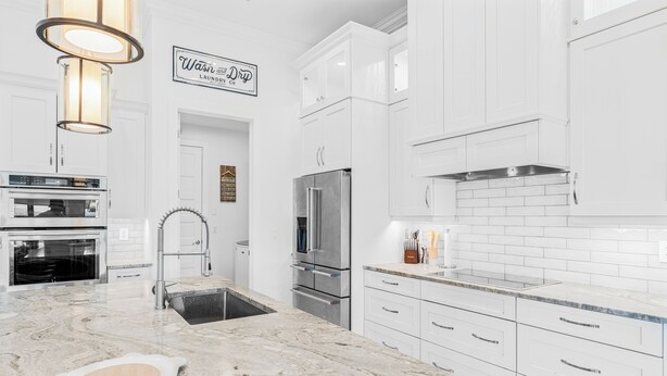 A modern kitchen with white cabinetry, a marble countertop, stainless steel appliances, and a sign above the door.