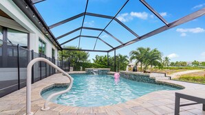 A swimming pool with a glass enclosure, stone tiles, and a hot tub.