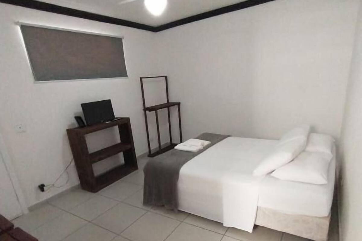 A small, clean room with a bed, a desk, and a ceiling fan.