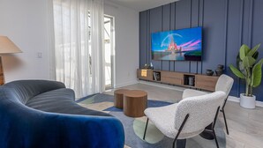 A modern living room with a curved blue sofa, a white armchair, a wooden coffee table, and a flat-screen TV mounted on a blue wall. - Spacious 4-bedroom townhome, perfect for family getaways! (Kissimmee)