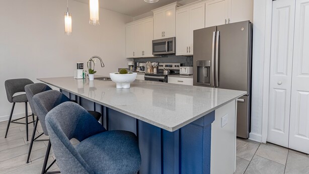 A modern kitchen with a central island, stainless steel appliances, and a white door. - Spacious 4-bedroom townhome, perfect for family getaways! (Kissimmee)