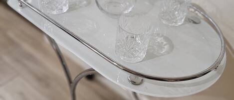 Uma bandeja de vidro transparente com uma jarra e copos sobre um suporte de metal.